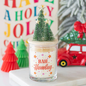Festive Bah Humbug Orange & Clove Christmas candle in glass jar with colourful design, wooden lid, and miniature Christmas trees topped with gold stars.
