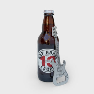 Stainless steel guitar-shaped bottle opener propped against a Hop House 13 Lager bottle, with product detailing clearly visible.