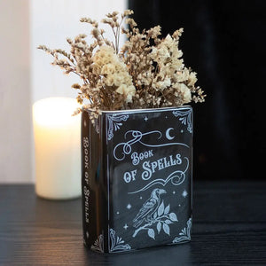 Book of Spells vase styled with dried flowers and candle. Ceramic Book of Spells gothic vase with dried flowers, styled on dark wood with glowing candle in background for moody home décor.