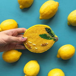 Fruity lemon beaded purse held in hand among fresh lemons on a turquoise background.