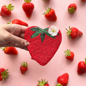 Fruity strawberry purse held in hand with matching strawberry-themed nails, surrounded by fresh strawberries.