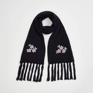 Fable Forget-Me-Not Knitted Navy Scarf with pink and blue floral embroidery and tassel fringe, laid flat on white background.