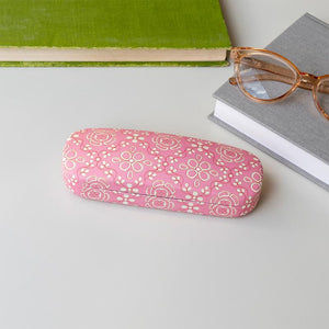 Front view of Anushka pink floral glasses case on a desk beside books and glasses.