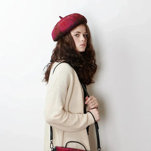 Festive Flair: A woman with a playful twinkle in her eyes looks to the side, her red tartan lambswool bunnet adding a pop of festive cheer to her winter outfit.
