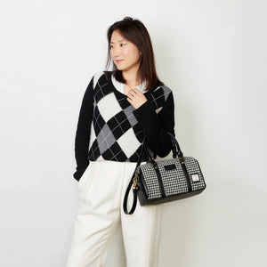 A woman holding a stylish black and white dogtooth patterned duffel bag. The bag is made from Harris Tweed®, a handwoven fabric from the Scottish Outer Hebrides. It has two sturdy carrying handles and a detachable shoulder strap.