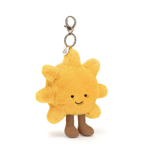 A cheerful Jellycat Amuseable Sun plush charm, crafted from golden soft fur and sporting a beaming smile, milk chocolate corduroy boots, and a handy silver chain and claw clip for attaching to bags, backpacks, or keys.