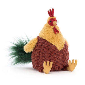 Jellycat Cluny Cockerel plush, a fluffy rooster with a cocoa tummy and yellow bib, viewed at a slight angle.