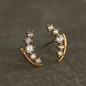 Close-up front view of gold vermeil stud earrings shaped like lily of the valley stems, each adorned with graduated white crystals on a stone-textured background.