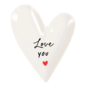 White trinket dish in the shape of a heart with the words love you printed in the middle. 