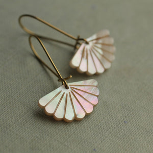 Close-up of gold-plated scallop earrings made from iridescent carved Mother of Pearl, displayed on a neutral fabric background.