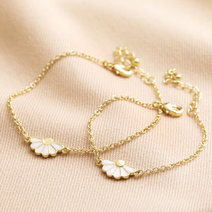Set of two gold-plated daisy bracelets with adjustable clasps on a soft fabric background.