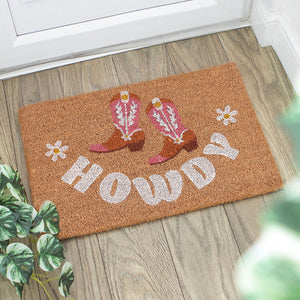 Howdy cowboy boot doormat on wooden floor at doorway with plants, perfect for rustic or western-themed homes.