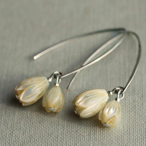 Close-up front view of carved mother of pearl snowdrop earrings on silver hooks, displayed on a soft grey fabric background.