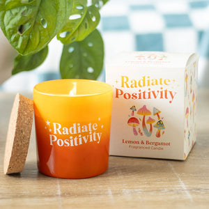 Radiate Positivity lemon & bergamot candle lit beside gift box with leafy background.