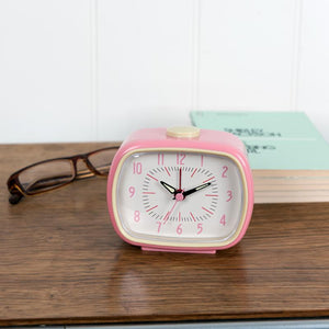 Retro pink alarm clock on a wooden desk with glasses and books – vintage-inspired bedside clock,