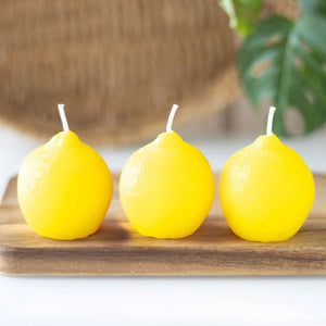 Set of three lemon-shaped novelty candles on a wooden board with tropical background — fun citrus-themed home decor.