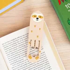 Sloth Reading Light clipped onto an open book – used as a bookmark with visible page detail.