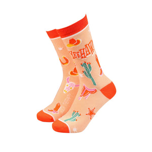 Women’s bamboo socks with bold western-themed design featuring cowboy hats, boots, cacti, and “Yeehaw” text on a peach background with bright red heel, toe, and cuff.