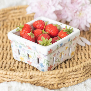Spring floral ceramic berry basket filled with fresh strawberries, styled on a woven placemat with soft florals in the background.
