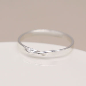 Sterling silver flat band ring with twist front detail on white surface.