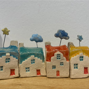 Assorted handcrafted ceramic houses from Edinburgh displayed on a rustic shelf with a soft-focus background.