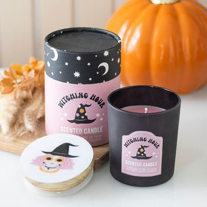 Front view of Witching Hour plum and black cherry scented candle in black glass with pink label and matching decorative box, styled with autumn décor.
