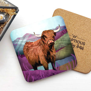 A Tartan Highland Cow coaster with a vibrant illustration of a Highland cow against a purple and green tartan-patterned background, placed on a white surface with a cork backing visible.