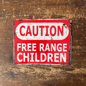 Flat lay of red Free Range Children warning sign on wooden background – 11x16 inch aluminium wall art for indoor or outdoor use.