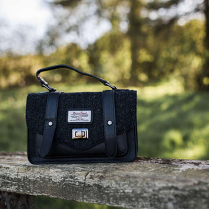 Harris Tweed bag in a forest setting with leather straps and black herringbone fabric.