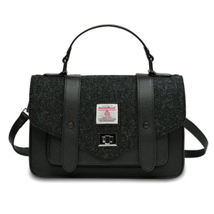 Islander Harris Tweed satchel style handbag in a Black Herringbone design. It has a black synthetic leather body and a shoulder strap lying behind.