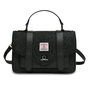 Islander Harris Tweed satchel style handbag in a Black Herringbone design. It has a black synthetic leather body and a shoulder strap lying behind. 