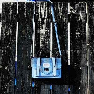 Light blue Harris Tweed Satchel shown handing at the side of a dock by its shoulder strap.