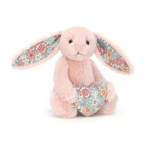 Jellycat Blossom Heart Blush Bunny is covered head to toe in baby pink fur and has floral patterned ears. It holds a heart between its paws.