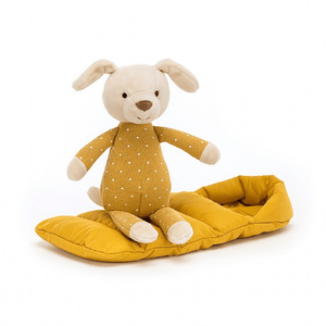 Jellycat Snugglers Puppy children’s toy wearing a yellow onesie and sitting on top of his yellow sleeping bag.