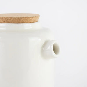 Close up image of the ceramic teapot in cream showing the spout and cork lid. 