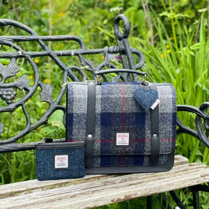 Harris tweed satchel in a blue and grey tartan sitting on a park bench.