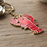 Coral red enamel lobster keyring with gold chain on wooden surface