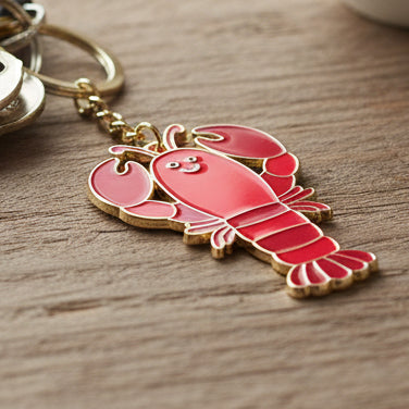 Coral red enamel lobster keyring with gold chain on wooden surface
