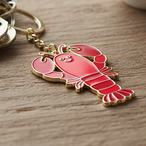 Coral red enamel lobster keyring with gold chain on wooden surface