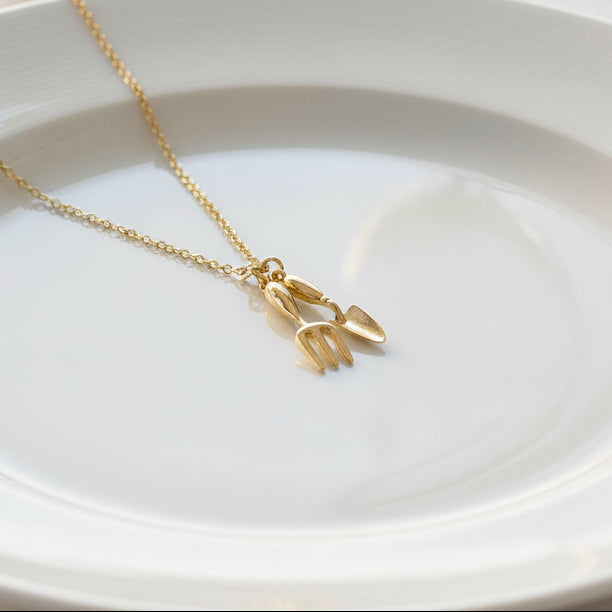 Spade and trowel pendant on gold-plated chain against white background