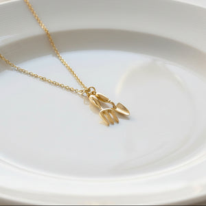 Spade and trowel pendant on gold-plated chain against white background