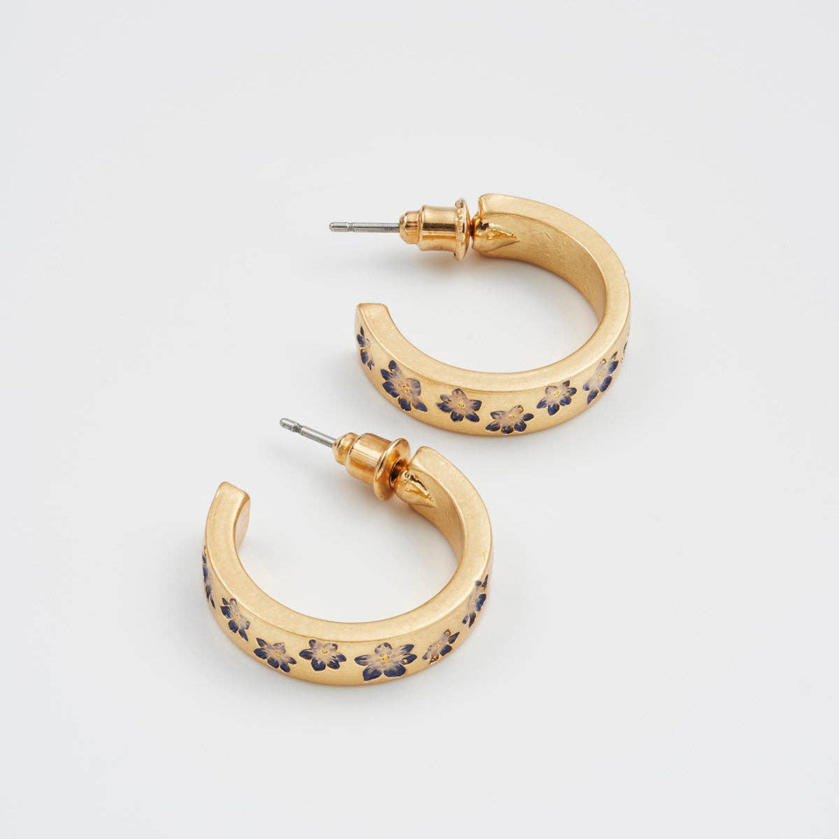 Gold hoop earrings with enamel florals laid diagonally on pale grey background