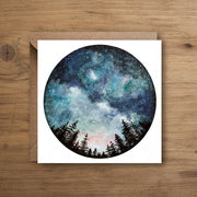 Card with a circular design of a starry night sky and trees, on a white background with a brown envelope.