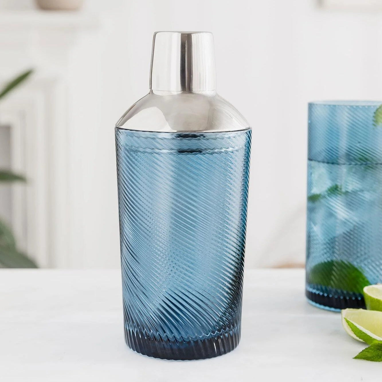Blue swirled cocktail shaker assembled with stainless steel lid on a white marble counter – elegant glass bar accessory
