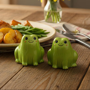 Two green frog salt and pepper shakers with smiling faces on a wooden dining table with potatoes and green beans