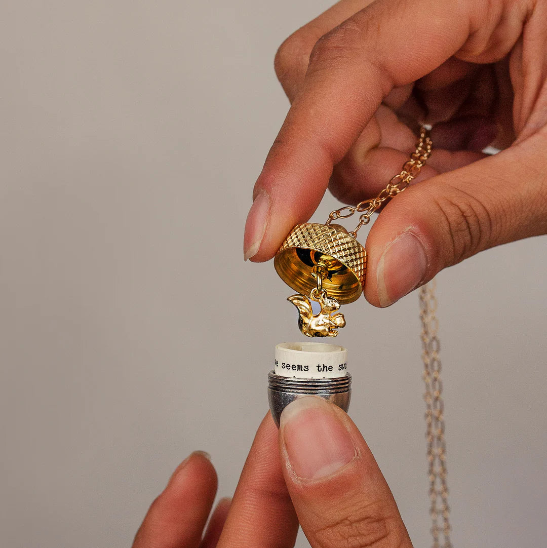 A close-up of the acorn locket being opened to reveal a personalised note and a small gold squirrel charm.