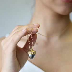 A woman wearing the Acorn Locket Necklace, displaying its elegant length and two-tone finish.