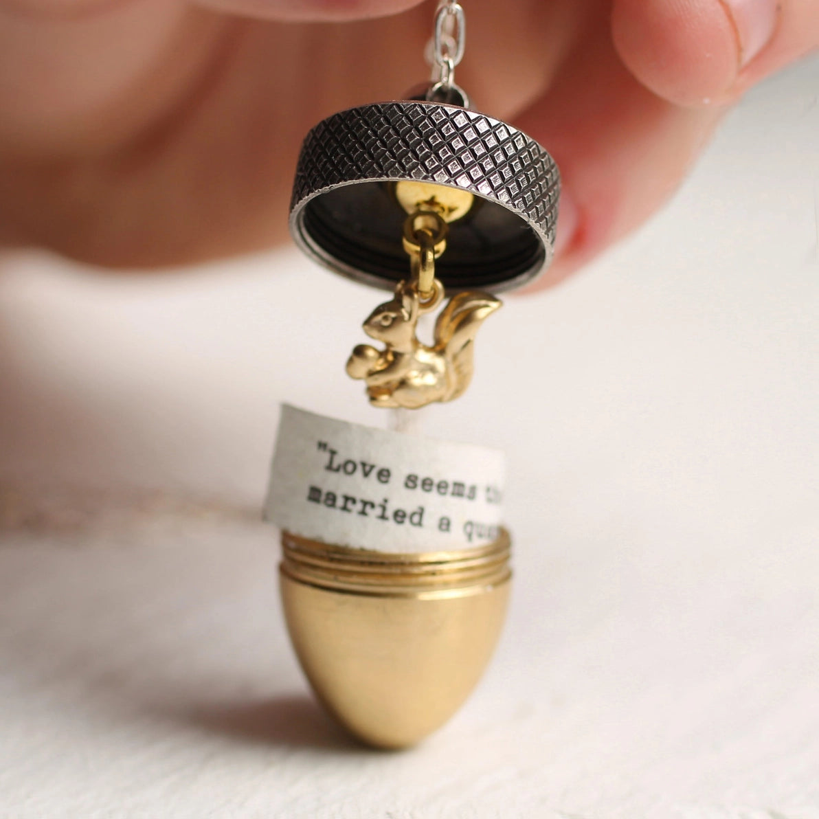 Close-up of a silver and gold acorn locket necklace being opened to reveal a tiny golden squirrel charm inside.