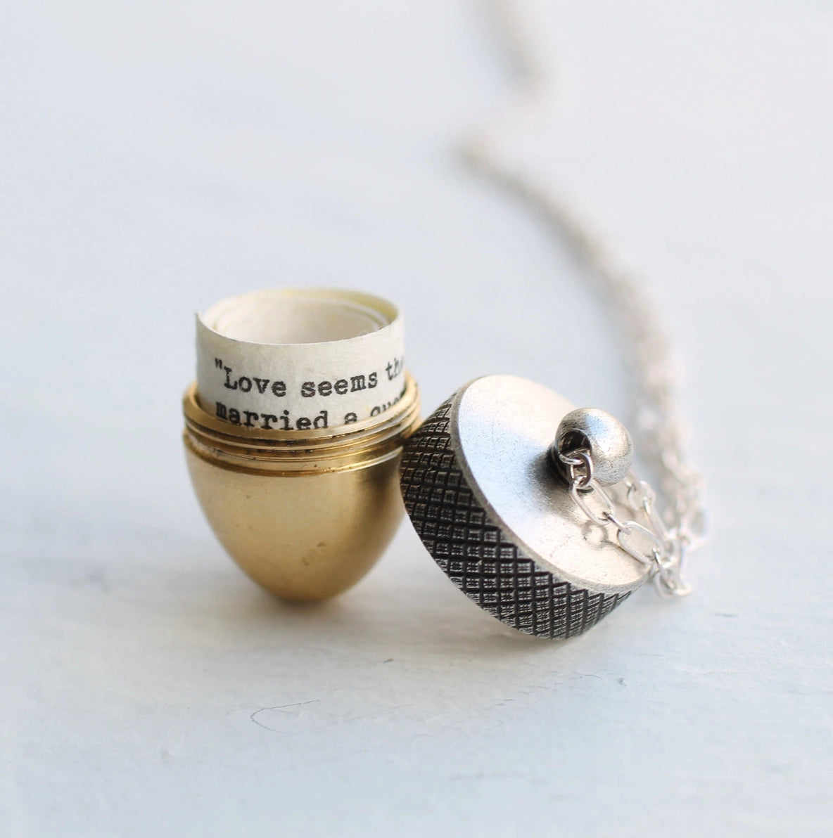 Opened acorn locket necklace with a silver top and gold bottom, revealing a hidden message scroll inside.