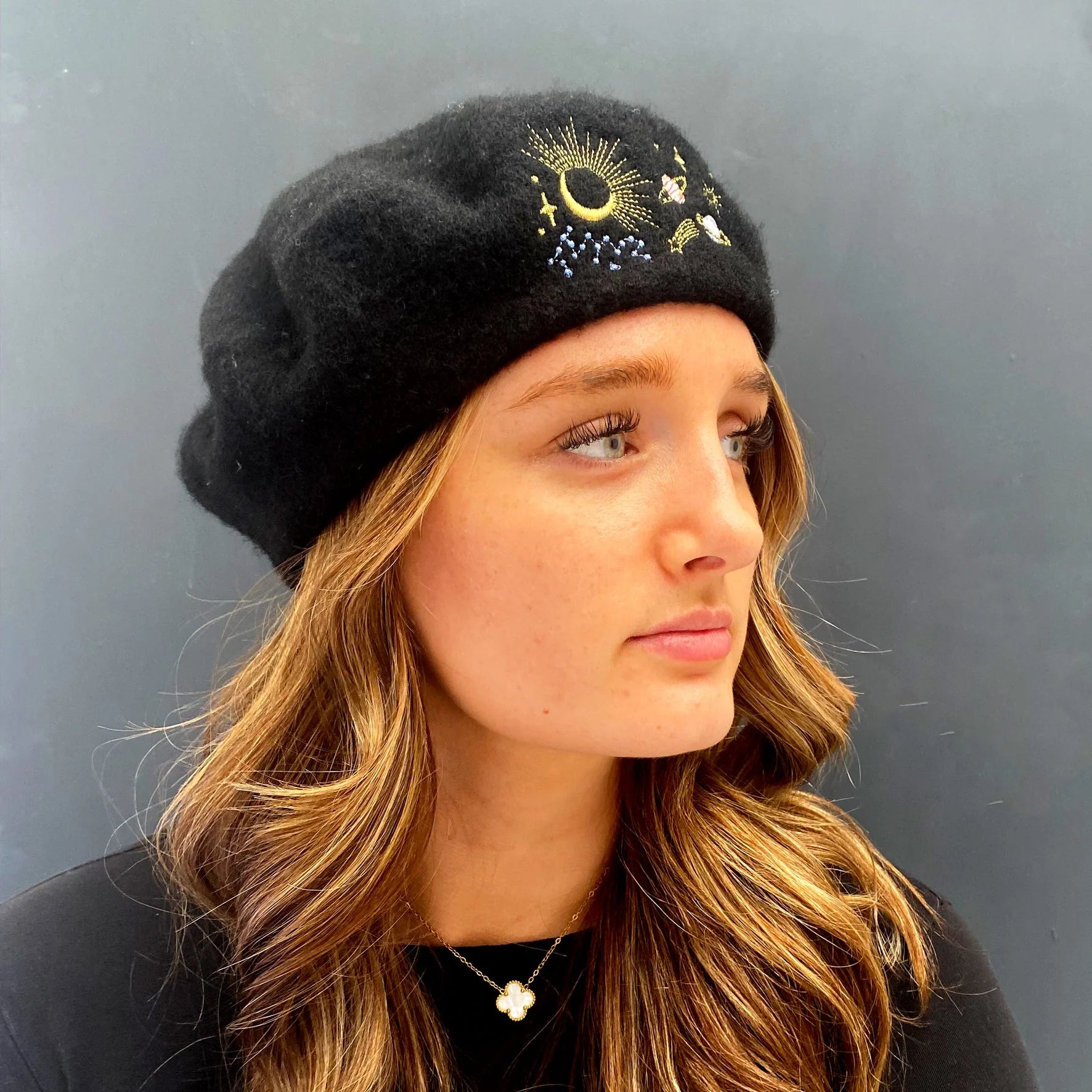 Side profile of woman wearing black wool beret with gold embroidered moon and stars.
